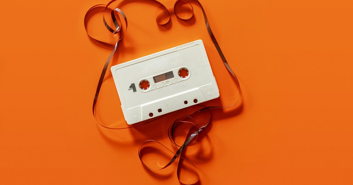 A white cassette tape with its loose tape unspooled across an orange background.