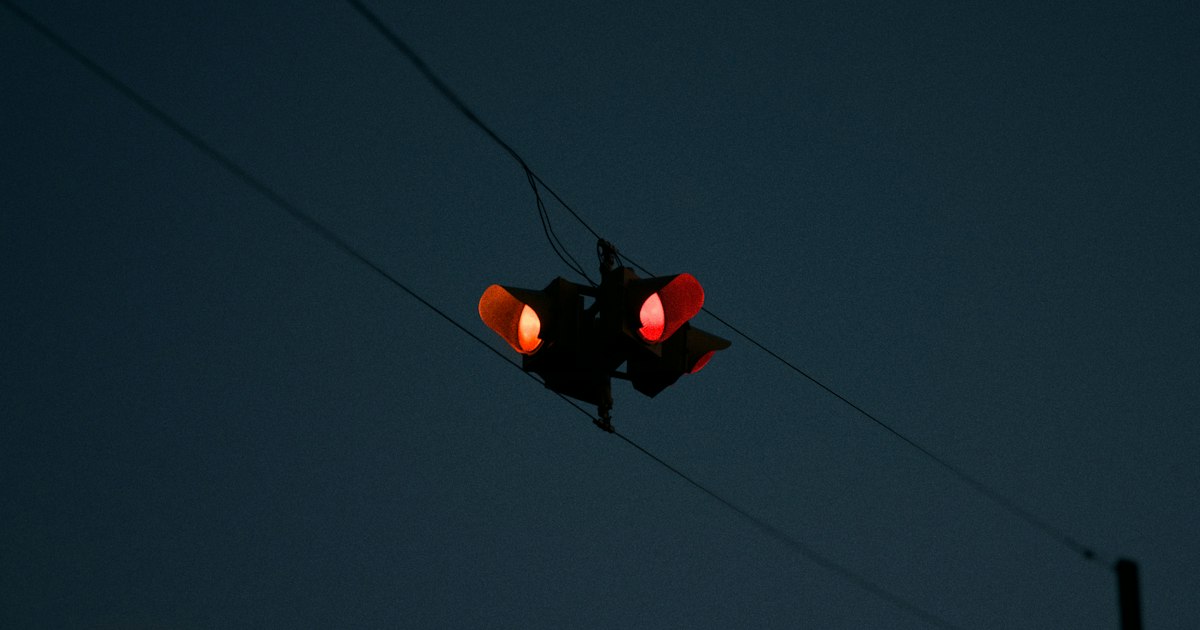 A single signal hanging from overhead wires glows red against a deep navy blue-hour sky.